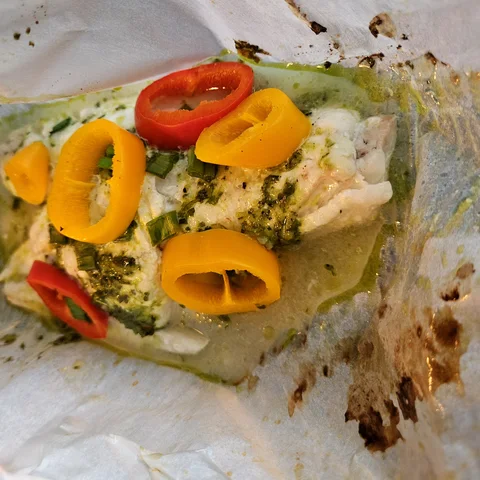 White fish baked in parchment with a green herb sauce and sweet pepper rings